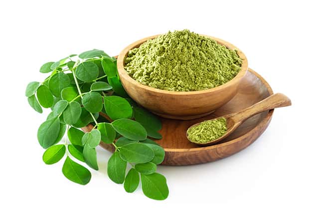 Moringa powder in a wooden cup with few moringa leaves
