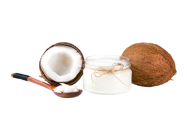 A Cup of virgin coconut oil and scoped spoon with few coconuts